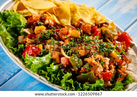 Grilled chicken meat with nachos and vegetables on wooden background
