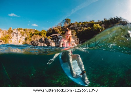 Happy surfer girl with surfboard. Surfer sit at board in ocean.