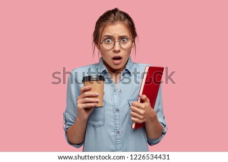 Puzzled emotional student wears spectacles, holds takeaway coffee and red textbook, fails final exam, feels frustrated as didnt enter prestigious university. Negative facial expression. Learning