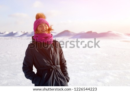 Winter warm photo. Portrait of a beautiful young model in knitted hat  and warm clothes smilling and walkingat the north pole, behind mountains covered in snow.  joyful cheerful mood.
