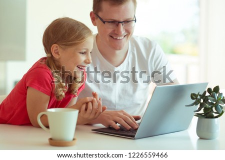Happy young father have fun with his pretty little daughter during working with laptop at modern home