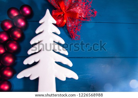 Merry Christmas greeting card, with white tree, blue wooden background, red colored balls, and various objects with space on the right where you can write a message