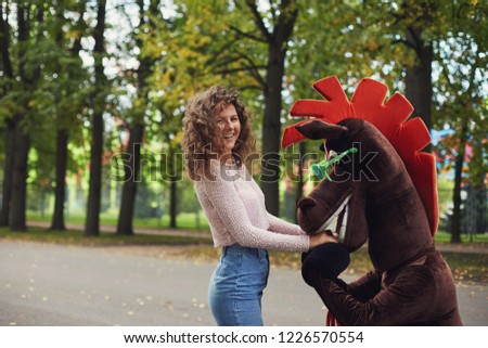 Outdoor positive shot of Caucasian beautiful woman smiling at camera, having fun together with cartoon hero. Authentic portrait of healthy female adult playing, laughing, having great vacation abroad.