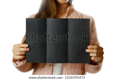A woman in a warm winter jacket holding a black leaflet. Blank paper. Close up. Isolated on white background.
