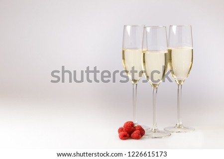 Stylish flutes of champagne with fresh ripe raspberries to toast a special occasion or holiday celebration over grey with copy space