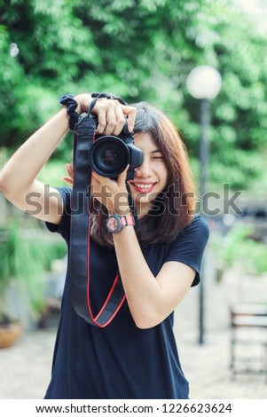 Beautiful and Happy Asian Woman holding Camera in the Garden.