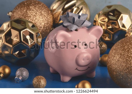Little pink piggy bank with a bow on the head close-up. Nearby are a lot of gold and silver Christmas balls of various sizes. The symbol of the new year. Holiday photography.
