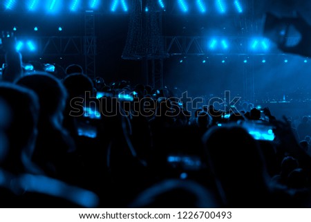 Concert field, crowded people and blue stage lights with smoke.