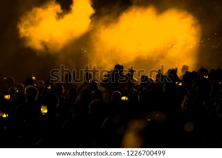 Concert field, crowded people and yellow stage lights with smoke.