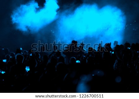 Concert field, crowded people and blue stage lights with smoke.
