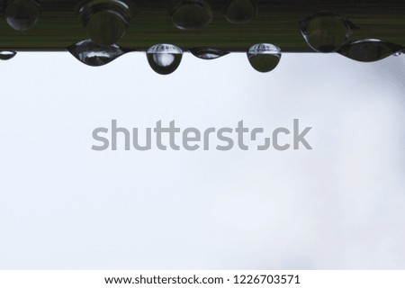 Rain water drops hanging on stainless steel metal bar reflected in the grass.
