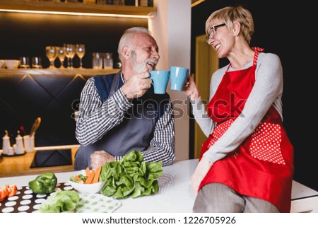 Senior couple talking, drinking coffee and preparing lunch together in kitchen.