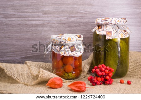 Salted tomatoes, Pickles  in glass jars and Rowan and physalis berries on a wooden background. Fermented vegetables.