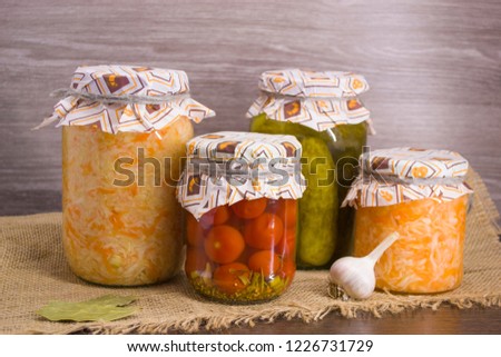 Pickles, salted tomatoes, salted cabbage in glass jars on a wooden background. Fermented vegetables.