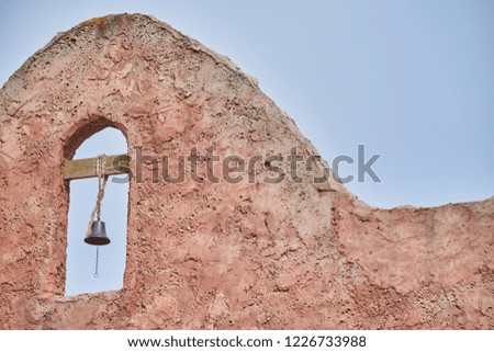 Photo of an old western style bell tower hung on a cement facade painted in brown and blue sky background