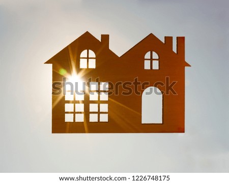 Male hand holding a wooden toy house with window and door against blue sunny sky. sun rays, beam. sun light. eco bio building