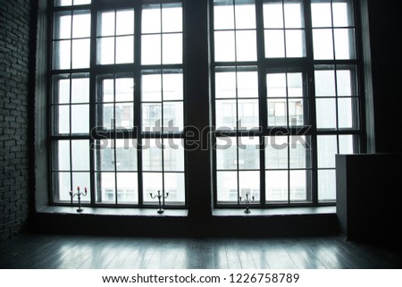 A big and wide window, interior in the studio or big building. Daylight outside, black and white picture.