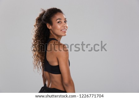 Back view portrait of a smiling young african sportswoman isolated over grey background, looking at camera