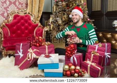 You only get this at Christmas. Delivery Christmas gifts. Guy is celebrating Christmas at home. Man in santa hat hold Christmas presents. Happy man with xmas gift boxes. The season to be jolly.