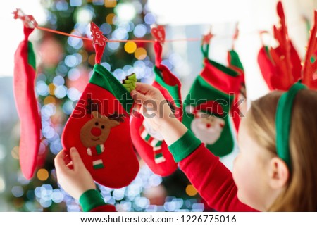 Kids opening Christmas presents. Child searching for candy and gifts in advent calendar on winter morning. Decorated Christmas tree for family with children. Little girl in Xmas pajamas.
