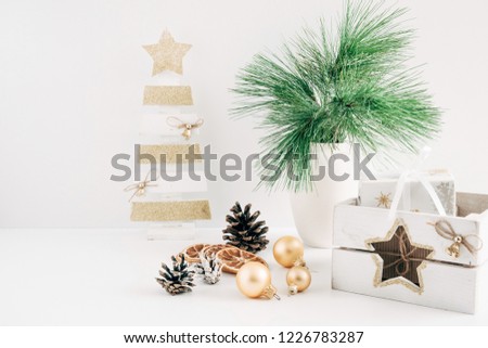 Home Decor, Interior. Decorative wooden Christmas tree, vase with fir branches, cones, Christmas decorations, gift on a white table.