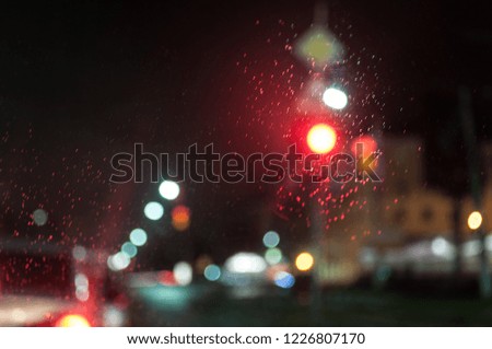 Red light. View through the windshield of the car. Raindrops on the glass. Blurry photo. Night in the city.