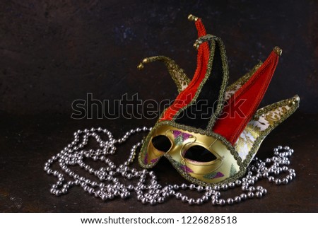 Carnival venetian Joker mask and silver beads on dark background. Carnival mask side view.