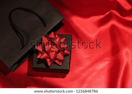 Black gift box and black shopping bag with space for text on red fabric; Background for black friday, shopping, promotion, holiday and discount.