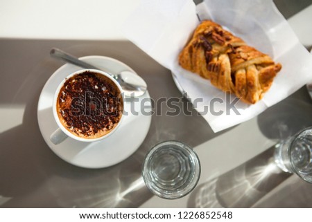 Close up, top view of coffee (espresso, cappuccino) on the table with bakery in the restaurant (Italian bar) with glass of water during the breakfast. Italy, Sicily
