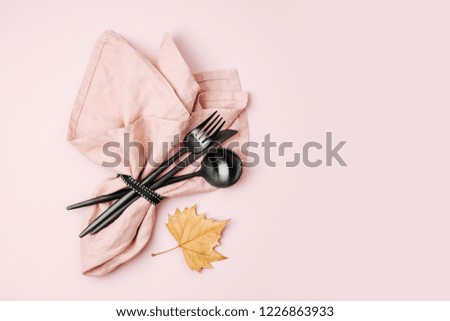 Black cutlery, pale pink napkin and autumn leaves on pastel background. Flat lay, top view