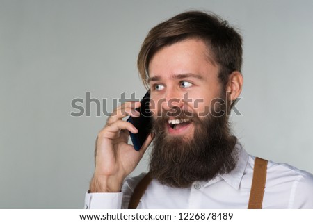 A man with a beard in a white shirt and yellow suspenders happy talking on the phone found the idea on a gray background