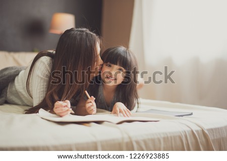 Love of young mother and daughter. Teaching reading a homework or book on the bed at home. mother kiss her daughter with smile feel good