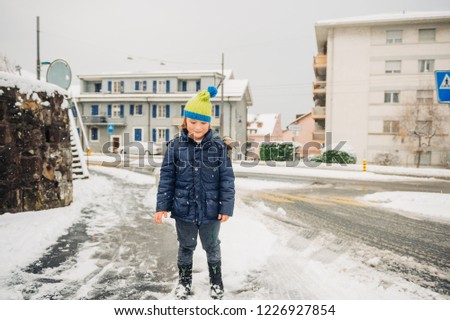 Outdoor portrait of young 6 year old boy wearing warm jacket and hat, enjoying winter time