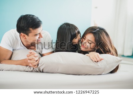 Young mother father and daughter enjoying with lie on the stomach in the bed, happy family smiling at home. daughter kiss mother