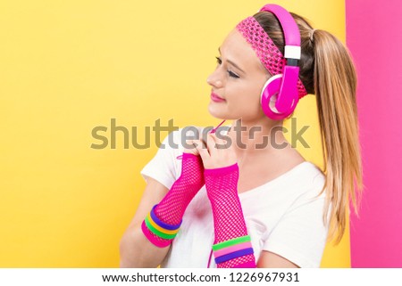 Woman in 1980's fashion with headphones on a split yellow and pink background