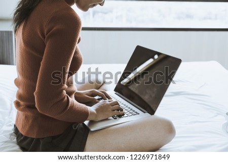 Young attractive woman using laptop while sitting on bed alone in living room during relax time. Women lifestyle concept