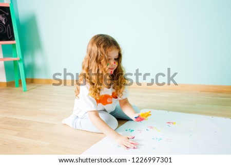Charming little girl painting using her fingers while sitting on the floor