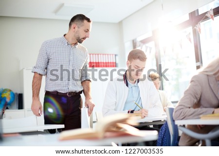 Serious teacher looking at one of students notes during individual work in class