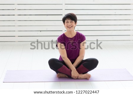 People, yoga, sport and healthcare concept - Relaxed smiling middle-aged woman sitting on exercise mat over white background