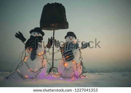 Funny decorated snowmen. Snowmen wearing a hat, mittens and a scarf in a snowy night. Christmas scenery in the winter landscape