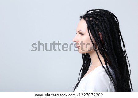 Cute young woman with dreadlocks on grey background