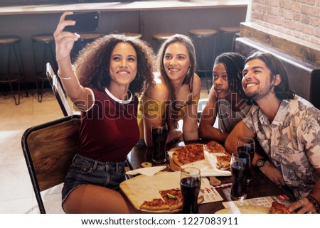 Young woman taking selfie with friends sitting at restaurant. Group of multi-ethnic friends at cafe capturing a selfie in smart phone.