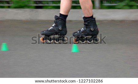 Boy riding on rollers in the summer park. Legs of boy on rollers, cropped image. Kid learning to roller skate on the road with cones.