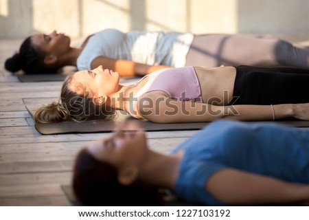 Group of young people practicing yoga lesson doing Dead Body, Savasana exercise, Corpse pose, working out, indoor close up, mixed race female students training at yoga studio. Well-being concept Royalty-Free Stock Photo #1227103192