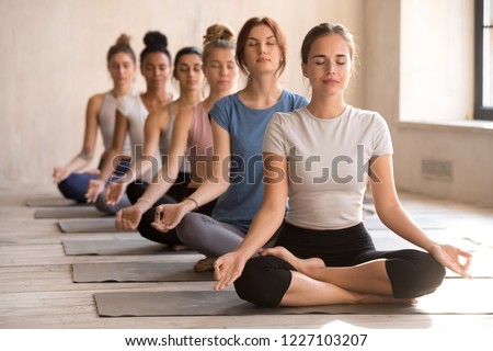 Group of diverse young people practicing yoga, doing Easy Seat exercise, Sukhasana pose, working out indoor full length, female students meditating at club or yoga studio. Well being, wellness concept Royalty-Free Stock Photo #1227103207