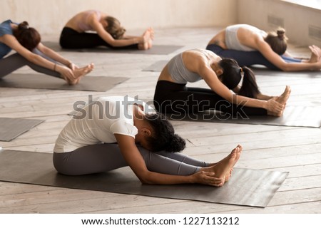 Group of young people doing yoga Seated forward bend exercise, paschimottanasana pose, working out, indoor full length, mixed race female students training at club. Well being, wellness concept Royalty-Free Stock Photo #1227113212