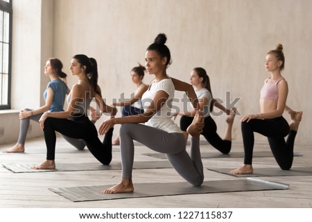 Group of diverse young sporty people doing Horse rider exercise, anjaneyasana pose, working out indoor, mixed race female students training, yoga lesson at club or studio. Well being, wellness concept Royalty-Free Stock Photo #1227115837