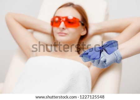 Underarm laser hair removal treatment woman. Process of preparing glasses from influence radiation.