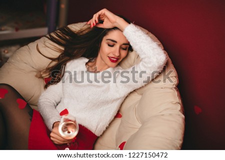 Tired long-haired woman in short skirt lies on sofa. Indoor shot of charming girl chilling in evening with wineglass.