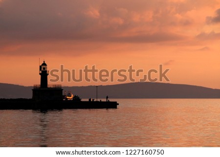 Lighthouse and fisherman on the dock. Beautiful sunset in the background, back lit. 